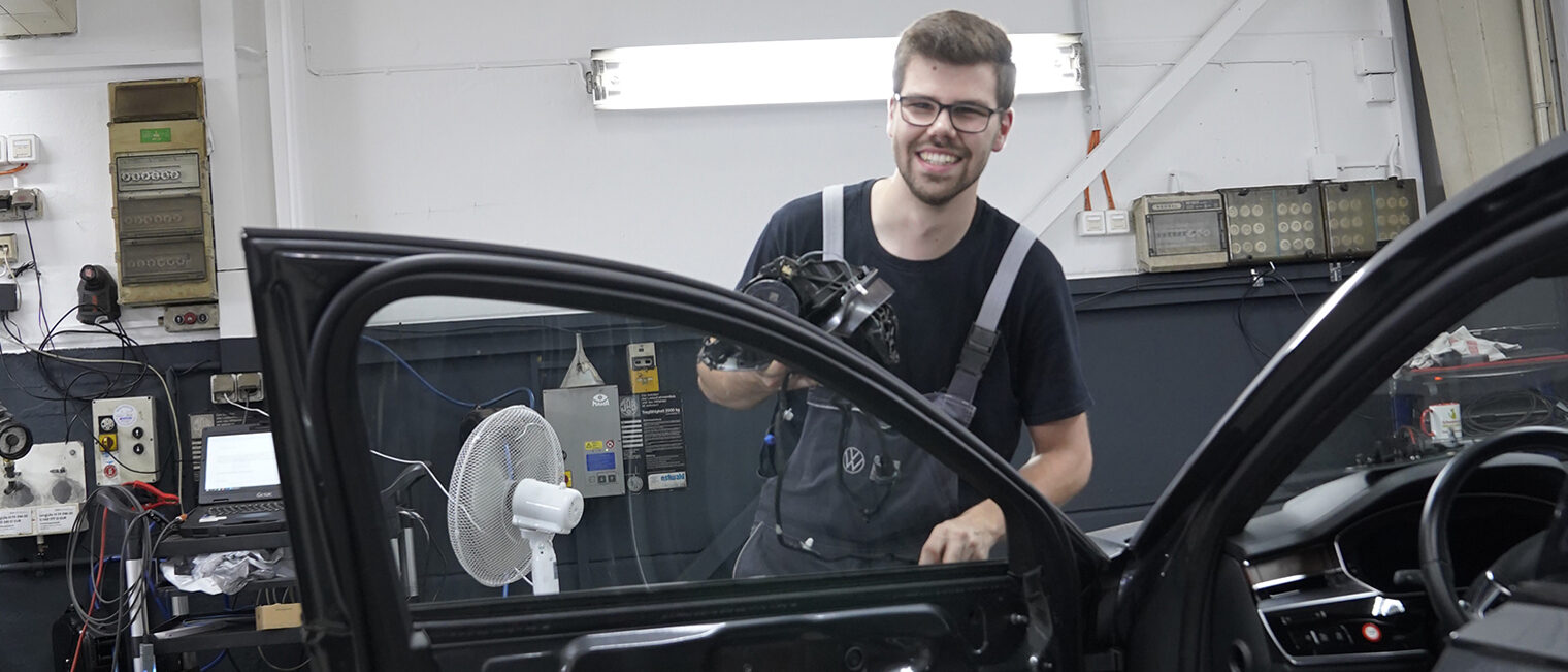 Lehrling des Monats Georg Wahl steht hinter einer geöffneten Autotür in der Kfz-Werkstatt.